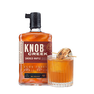 A bottle of Knob Creek Smoked Maple Whiskey next to a cocktail in a low ball glass
